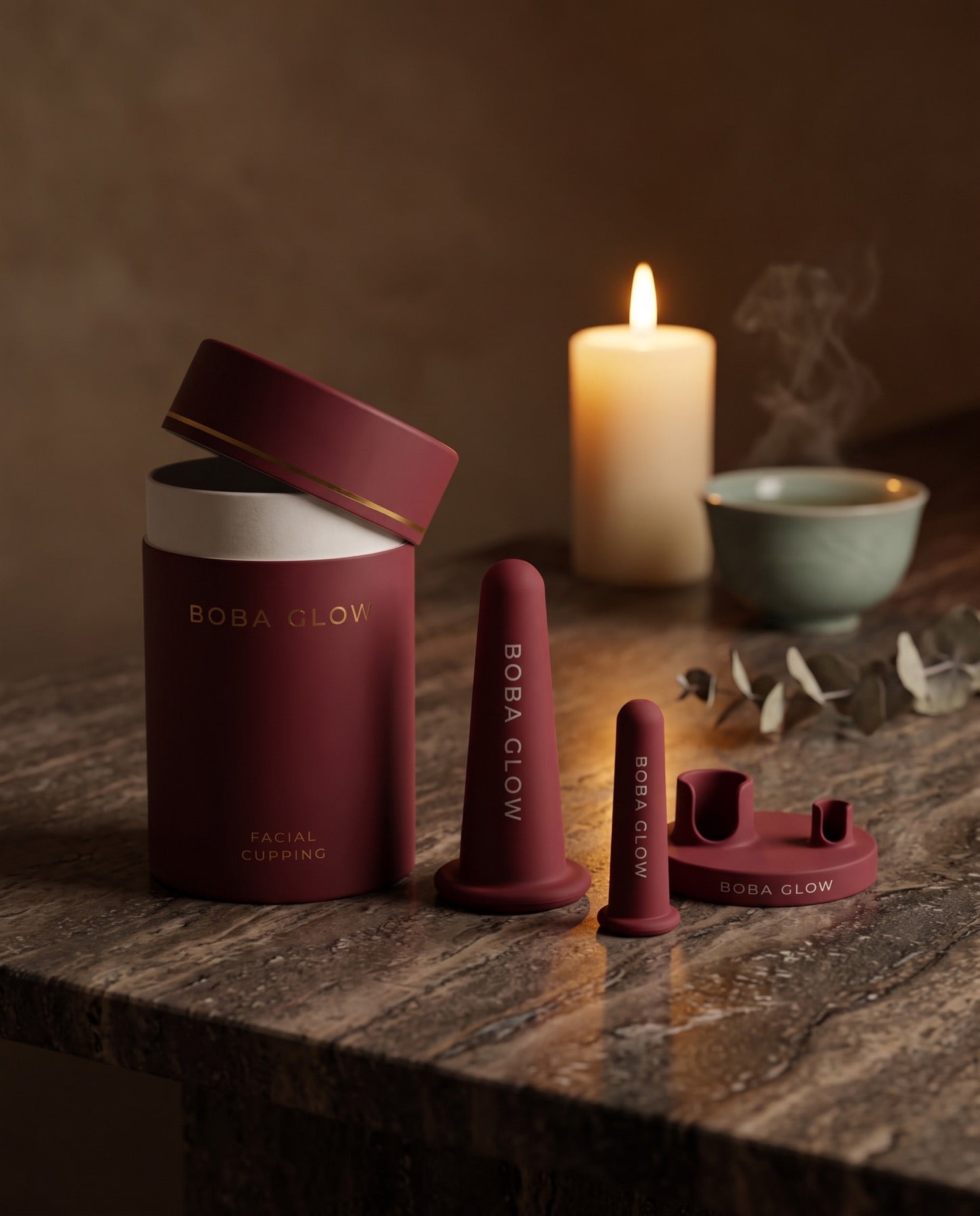 The BOBA GLOW cupping set on dark stone in warm candlelight, beside a ceramic tea bowl